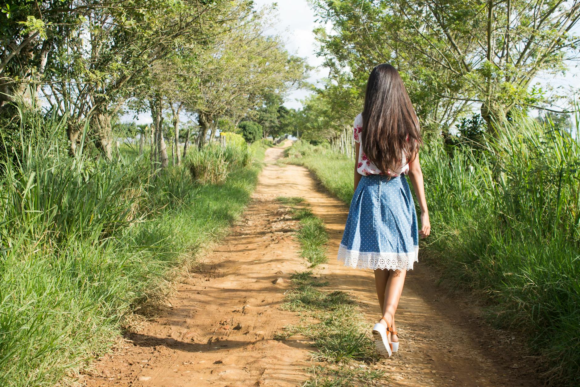 woman wearing blue and white skirt walking near green grass during daytime